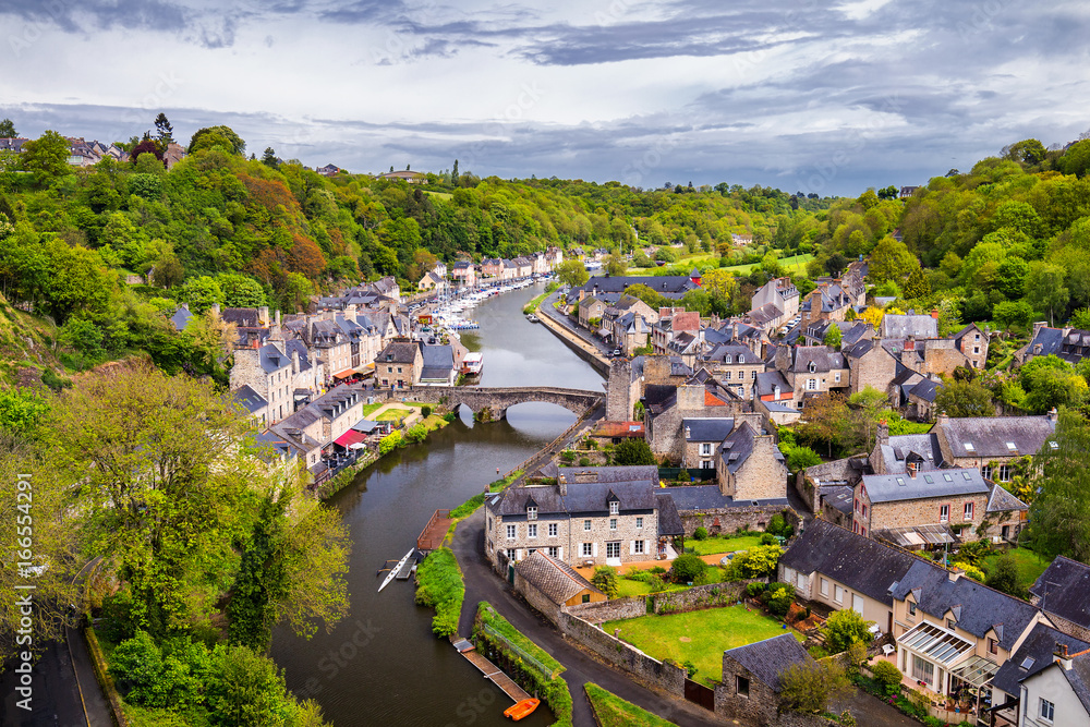Obraz premium Beautiful view of scenic narrow alley with historic traditional houses and cobbled street in an old town of Dinan with blue sky and clouds. Brittany (Bretagne), France