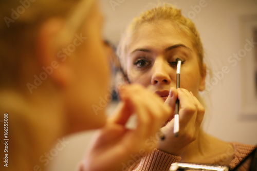 Beautiful blonde woman putting eye shadow in her bedroom in the morning.