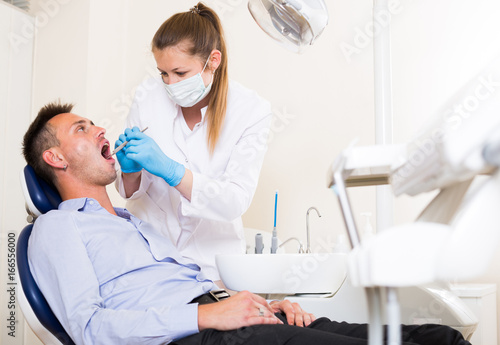 Stomatologist in uniform is taking visional inspection of a man on the chair