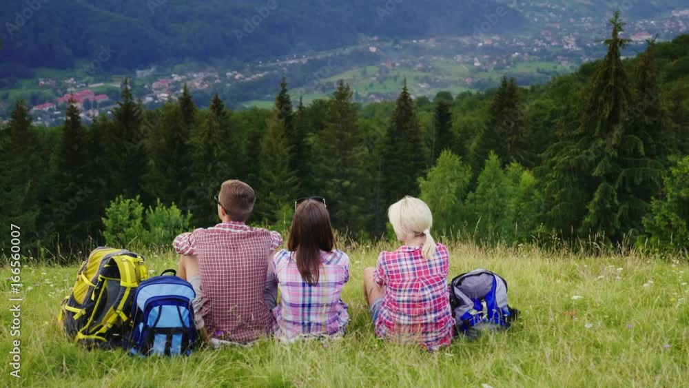 Crane shot: Friends of tourists sit in a picturesque place in the background of the mountains. They rest, admire the beautiful scenery Crane shot: Friends of tourists sit in a picturesque place in the background of the mountains. They rest, admire the beautiful scenery