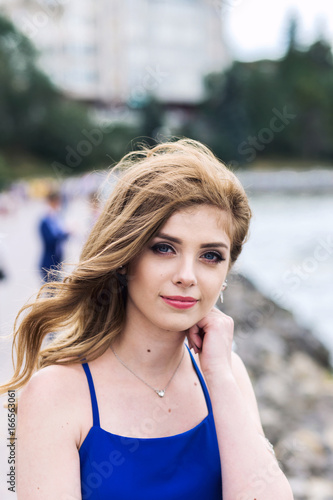 Portrait of a beautiful woman in a blue dress near a city lake