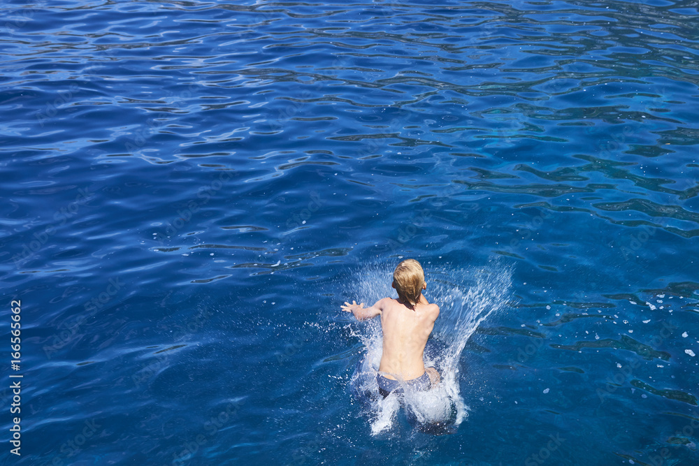 The child boy is jumping into the blue sea