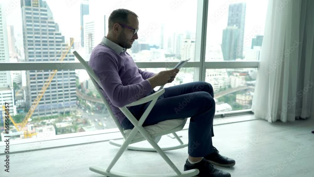 Young man reading documents sitting in rocking chair by window at home
Young man reading documents sitting in rocking chair by window at home