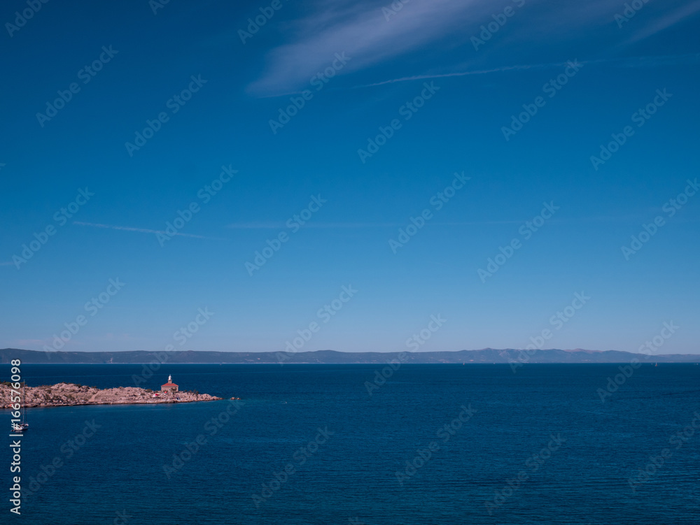 Calm blue sea and lighthouse on rocky coast