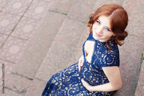 Beautiful young red hair pregnant woman sitting on stairs and touching big belly