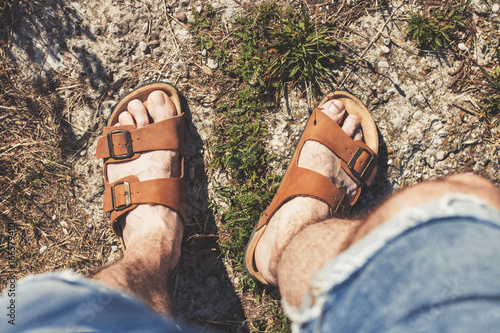 Top view of male legs in brown leather sandals and blue jean shorts, standing on a rocky trail photo