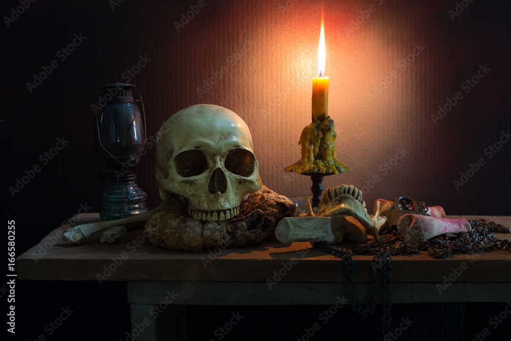 Still Life of skull and bone with fetters and candle on the wooden plank in dim light night Still Life of skull and bone with fetters and candle on the wooden plank in dim light night