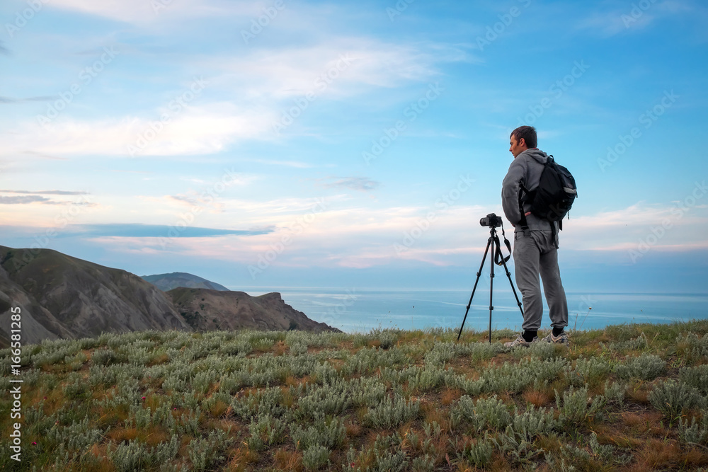 A photographer with a tripod and camera makes photos of landscapes on the mountain. Man in work.