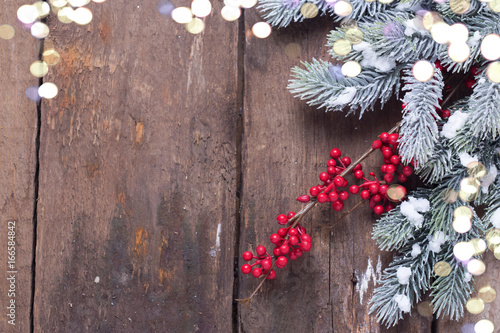 Spruce branches, decorative berries and holiday light  on aged wooden  background.