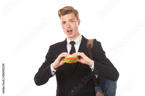 Portrait of college student in black suit eating sandwich against white background