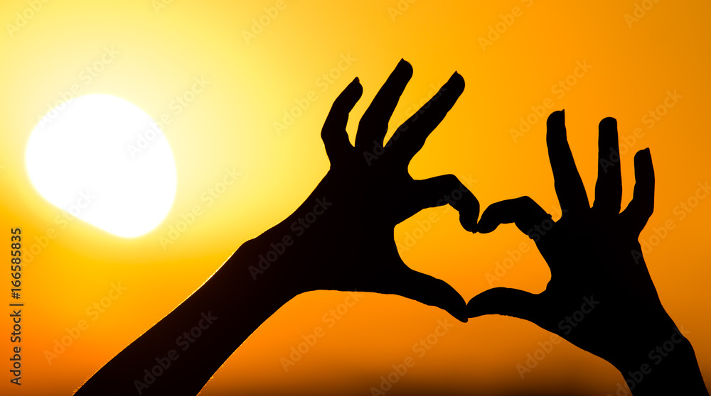 Silhouette of the heart by hands at sunset