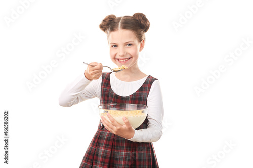 Portrait of cute girl in school uniform eating cereal with milk against white background