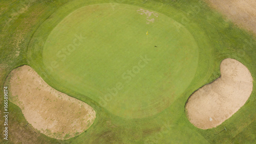 Vista aerea della bandiera gialla e della buca finale di un campo da golf in un centro sportivo a Roma, in Italia. Sullo sfondo due ostacoli formati da una buca di sabbia per complicare il gioco. photo