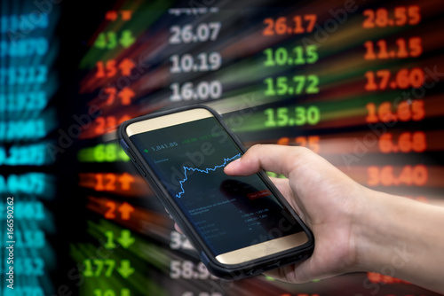 Stock Market Application for Mobile, Analyzing Data Stock Market on Mobile Young Businessman with Smartphone and Stock Market Chart Background.