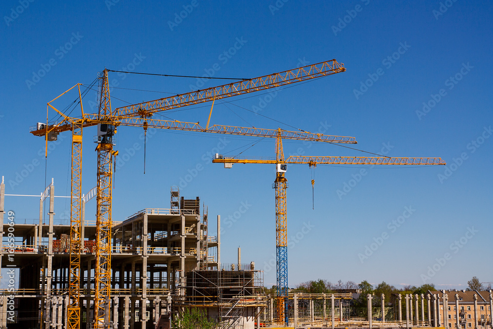 Construction tower cranes and high-rise building under construction against blue sky