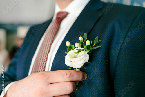 Groom is pinning a boutonniere to a suit. Wedding preparation photo