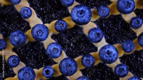 Excellent top-view of pie with rhombic pattern, violet jam and fresh blueberries close up, rotating contra clockwise. Amazing dessert with vibrant texture in 4k, 3840x2160, clip.
