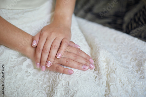 Hands of the bride with a manicure on a white dress