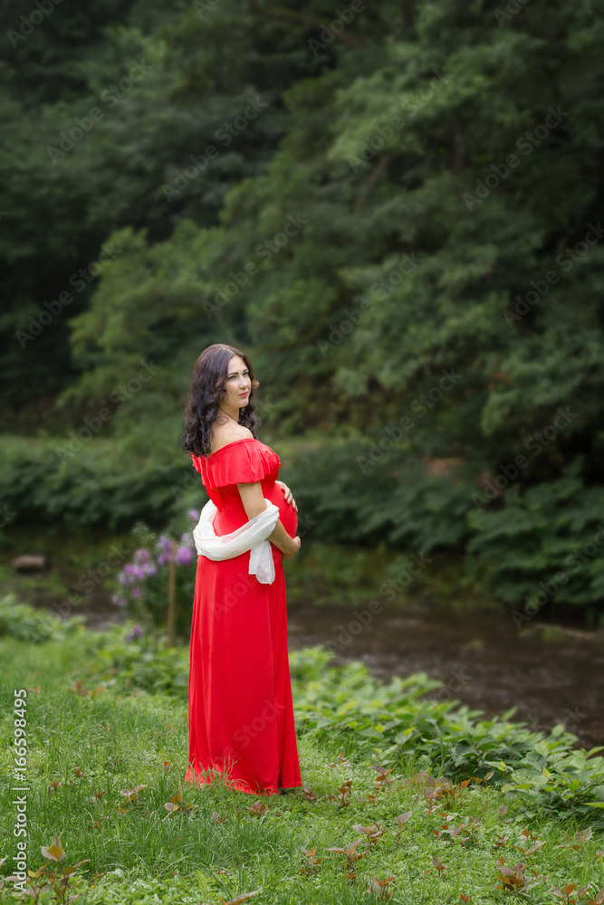 Pregnant woman in red dress in the park.