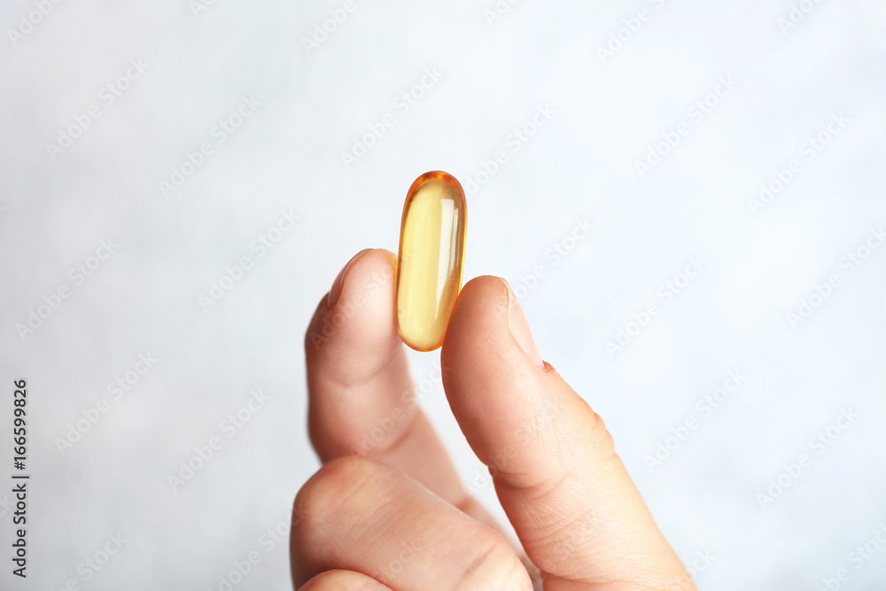 Fish oil pill in female hand on light background Fish oil pill in female hand on light background