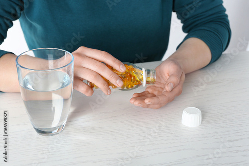 Woman pouring fish oil capsules from bottle into hand at table