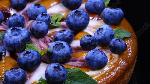 Excellent round pie with fresh whole blueberries and mint leaves, rotating clockwise with side center. Amazing dessert on black background with vibrant texture in 4k, 3840x2160, clip.
