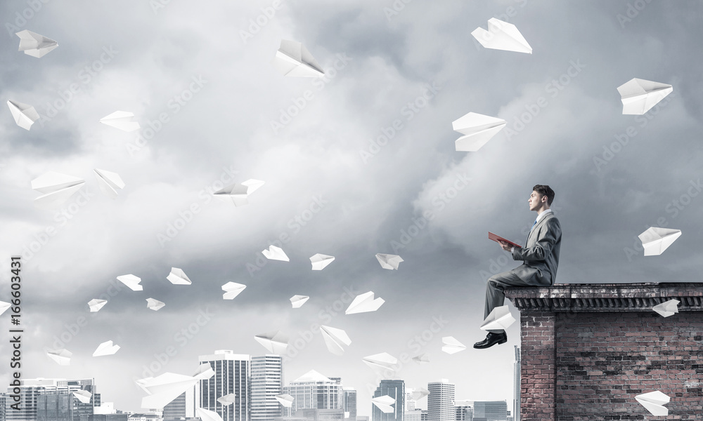 Man on roof edge reading book and cityscape at background Man on roof edge reading book and cityscape at background
