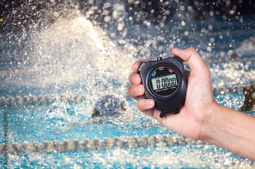 Stopwatch holding on hand with competitions of swimming background.