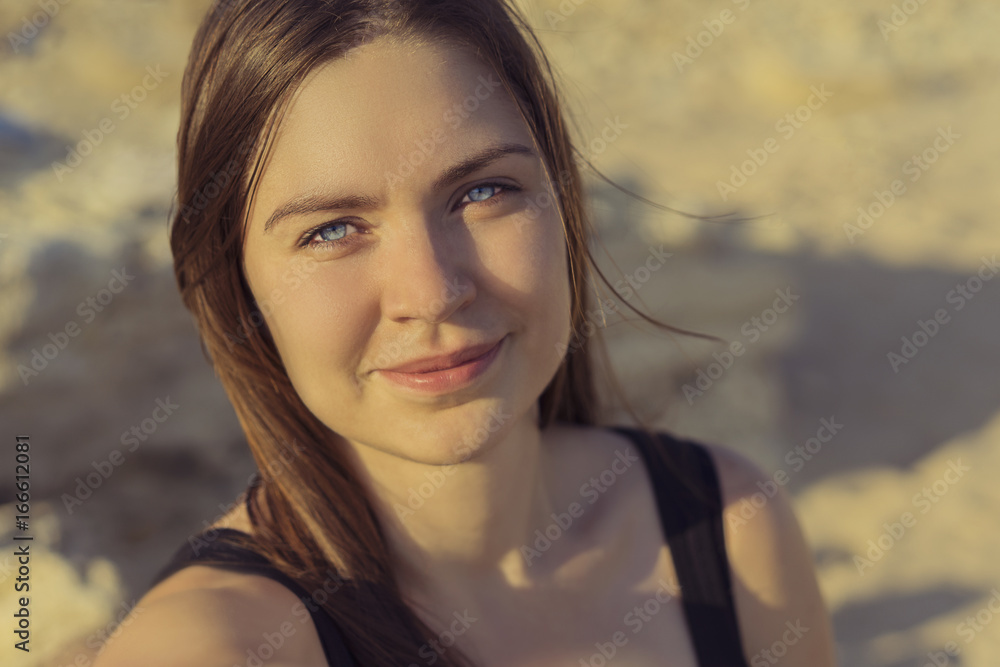 Portrait of beautiful smiling girl looking at camera with joyful and charming smile on a background of a sandy beach at sunset Portrait of beautiful smiling girl looking at camera with joyful and charming smile on a background of a sandy beach at sunset
