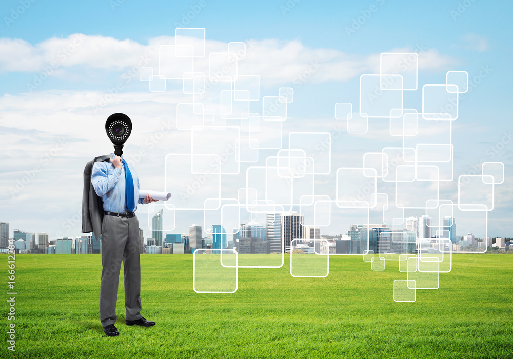 Camera headed man standing on green grass against modern cityscape Camera headed man standing on green grass against modern cityscape