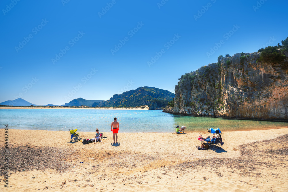Family having vacations at beautiful yellow sand of pristine famous Voidokilia beach attraction in Greece. Summer sunny day skyline scenery. Popular travel landmark and vacation destination.