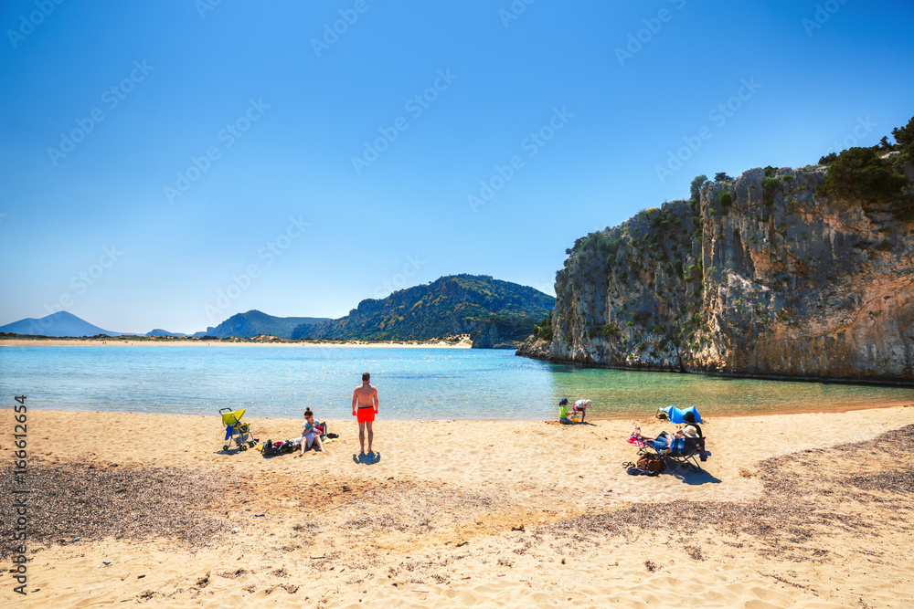 Family having vacations at beautiful yellow sand of pristine famous Voidokilia beach attraction in Greece. Summer sunny day skyline scenery. Popular travel landmark and vacation destination. Family having vacations at beautiful yellow sand of pristine famous Voidokilia beach attraction in Greece. Summer sunny day skyline scenery. Popular travel landmark and vacation destination.