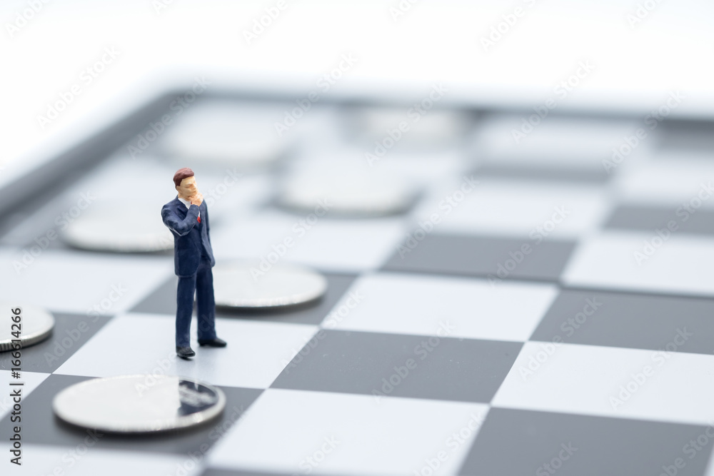 Businessman miniature people figure standing on chessboard with silver coins on black. Business, planning and work concept. Businessman miniature people figure standing on chessboard with silver coins on black. Business, planning and work concept.