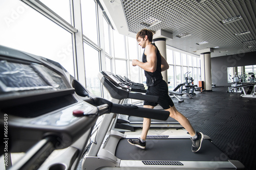 Young man in sportswear running on treadmill at gym. side view