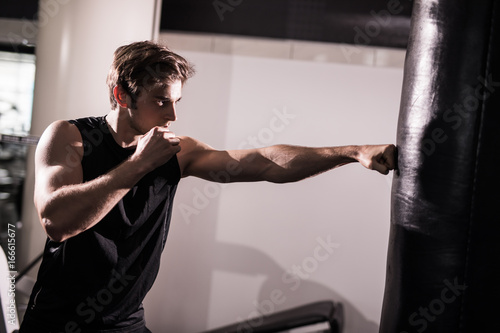 Young athlete working out by throwing punches at a heavy punching bag in gym. Training