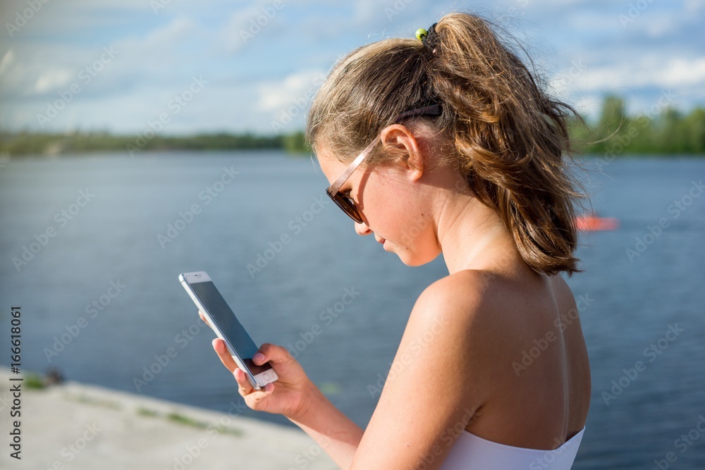 Young cute teen girl reading sms on her smartphone, view from behind.
