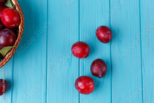 Four fresh plums on light blue table near basket. Delicious juicy fruits