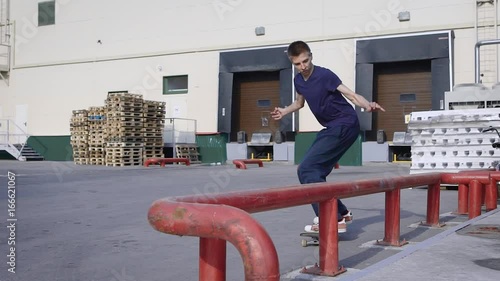 Teenager is jumping and making grind trick on skateboard along red railing in skaterpark. Skateboarder doing nosegrind on funbox outdoors. Boy spending time practicing summer extreme sport. photo