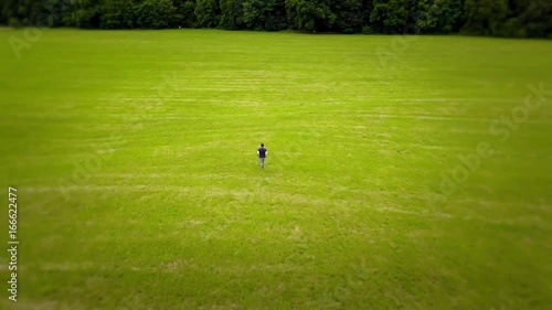 Young man quickly runs on a green field - Aerial view