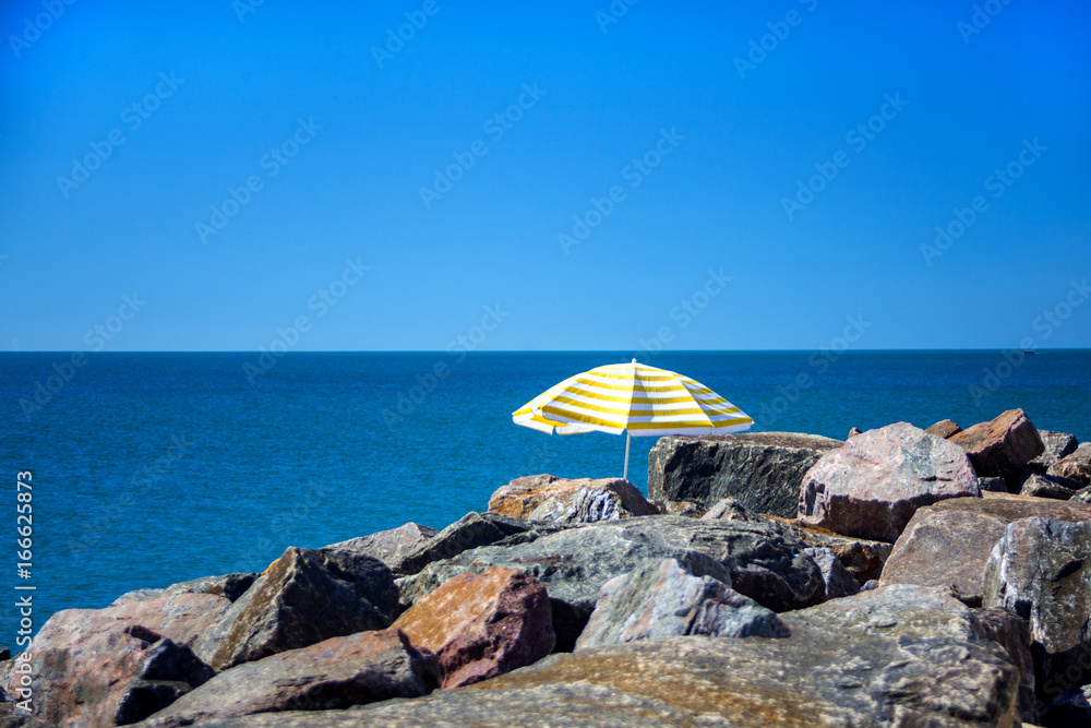 Lonely umbrella standing in stones on a wild beach