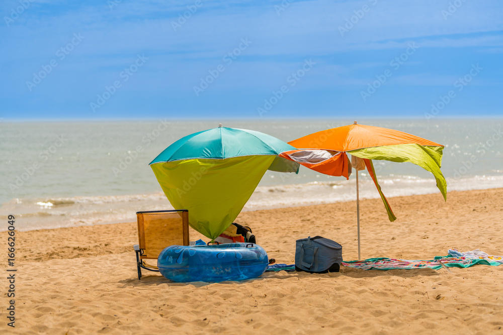 Two colorful sun parasols and a chair at a windy sunny beach in Algarve Portugal. Two colorful sun parasols and a chair at a windy sunny beach in Algarve Portugal.