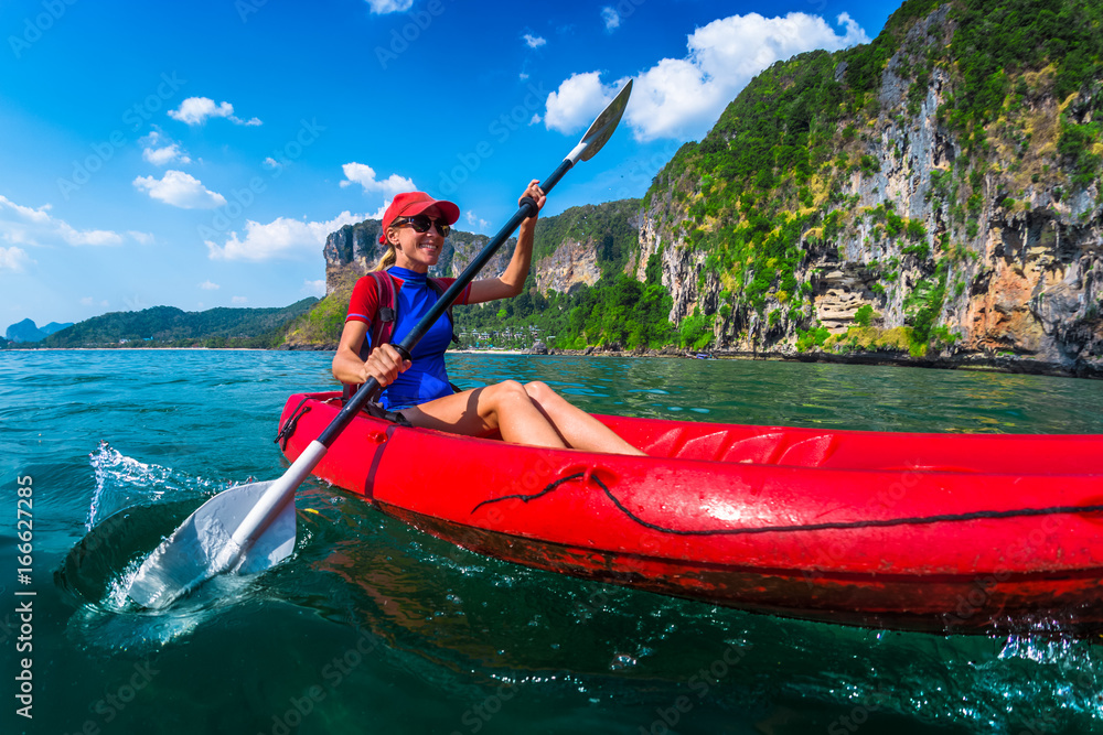 Woman paddles red kayak in a tropical sea