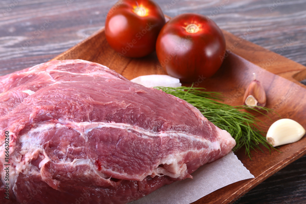 Raw pork steaks on wooden board with herbs, garlic, spices and tomatoes ready for cooking. Selective focus. Raw pork steaks on wooden board with herbs, garlic, spices and tomatoes ready for cooking. Selective focus.