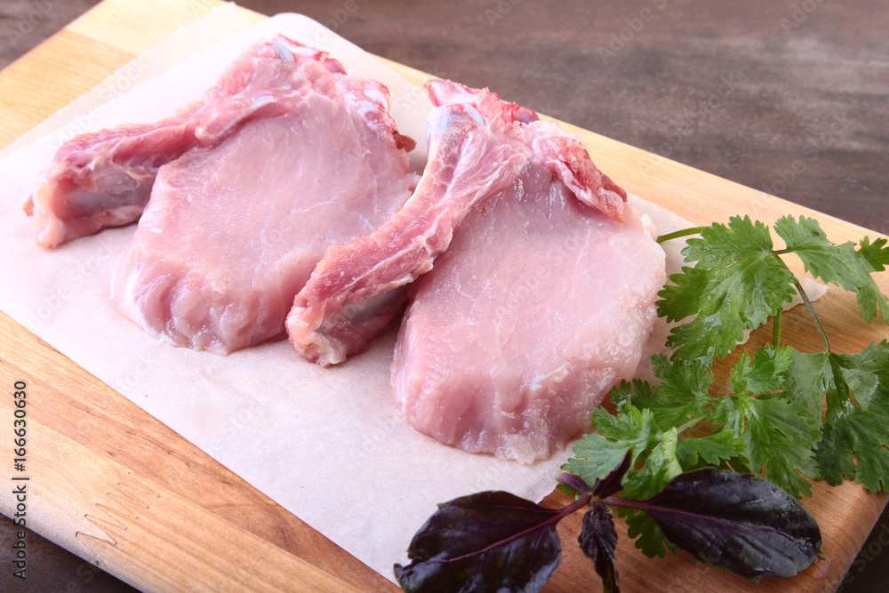 Raw pork steak with spices Leaves of coriander on wooden cutting board. Ready for cooking. Raw pork steak with spices Leaves of coriander on wooden cutting board. Ready for cooking.