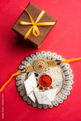 Raksha Bandhan greeting - Rakhi and gift with sweet kaju katli or mithai and rice grains & kumkum in a decorative plate. Traditional Indian wrist band is a symbol of love between Brothers and Sisters