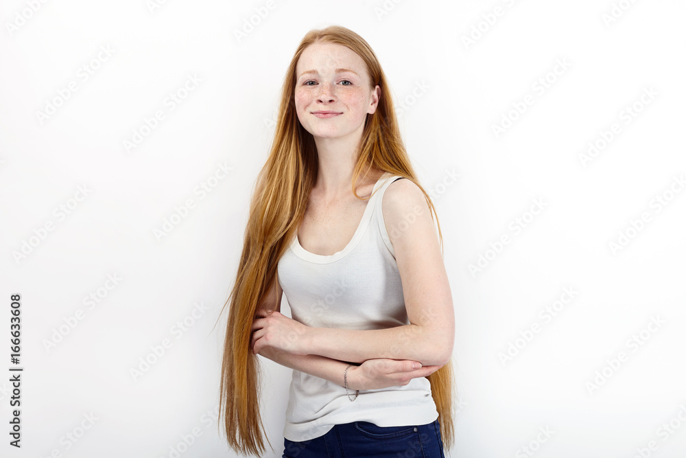 Young beautiful redhead beginner model woman in white t-shirt blue jeans practicing posing showing emotions standing against white wall background Young beautiful redhead beginner model woman in white t-shirt blue jeans practicing posing showing emotions standing against white wall background
