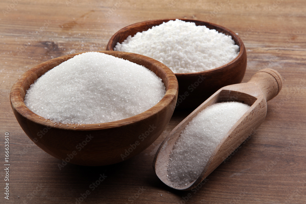 Bowl and scoop with white sand and lump sugar on brown wooden background Bowl and scoop with white sand and lump sugar on brown wooden background