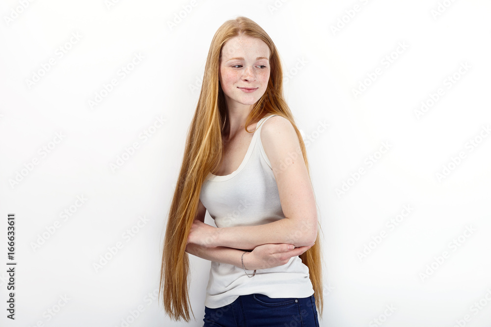 Young beautiful redhead beginner model woman in white t-shirt blue jeans practicing posing showing emotions standing against white wall background Young beautiful redhead beginner model woman in white t-shirt blue jeans practicing posing showing emotions standing against white wall background