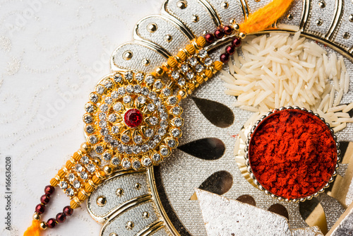 Raksha Bandhan greeting - Rakhi and gift with sweet kaju katli or mithai and rice grains & kumkum in a decorative plate. Traditional Indian wrist band is a symbol of love between Brothers and Sisters