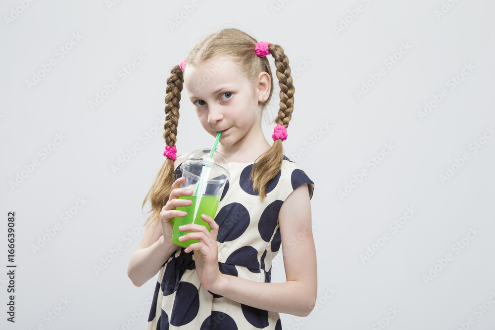 Portrait Of Cute And smiling Caucasian LIttle Girl With Pigtails Posing in Polka Dot Dress with Cup of Greeen Juice. Drinking Through Straw. Portrait Of Cute And smiling Caucasian LIttle Girl With Pigtails Posing in Polka Dot Dress with Cup of Greeen Juice. Drinking Through Straw.